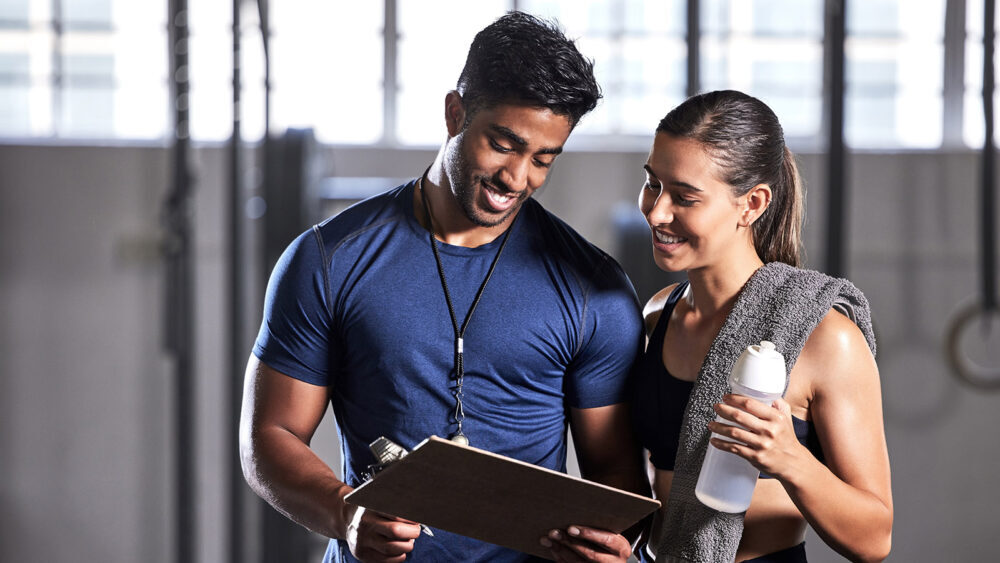 Gym subscription, personal trainer and happy client talking and ready to fill in a membership form. Fitness coach discussing training, workout plan and progress in a health and wellness facility