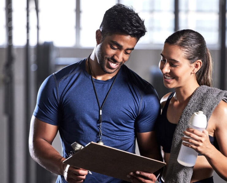 Gym subscription, personal trainer and happy client talking and ready to fill in a membership form. Fitness coach discussing training, workout plan and progress in a health and wellness facility